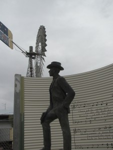 A.B. Paterson statue against backdrop of a huge windmill and grey skies.